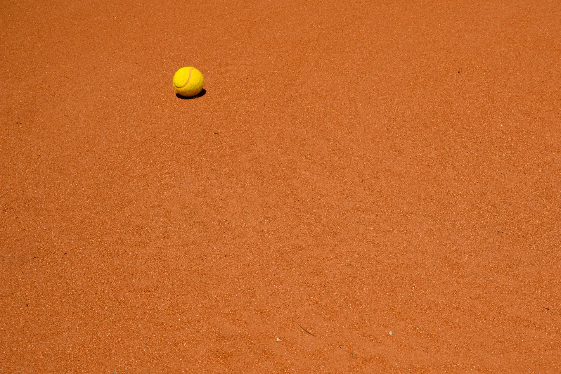 A single tennis ball resting on an orange clay court