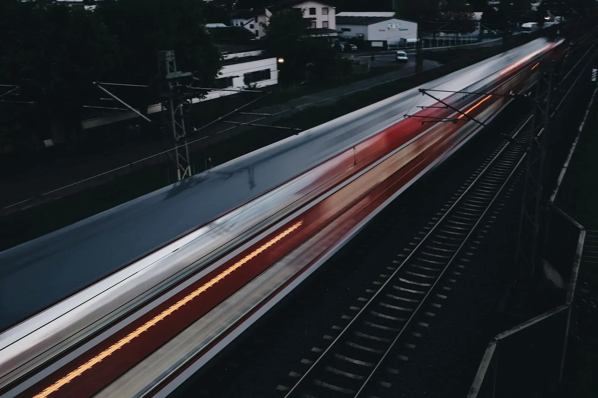 A train streaking past at dusk in a long exposure, red and white light trails over the tracks