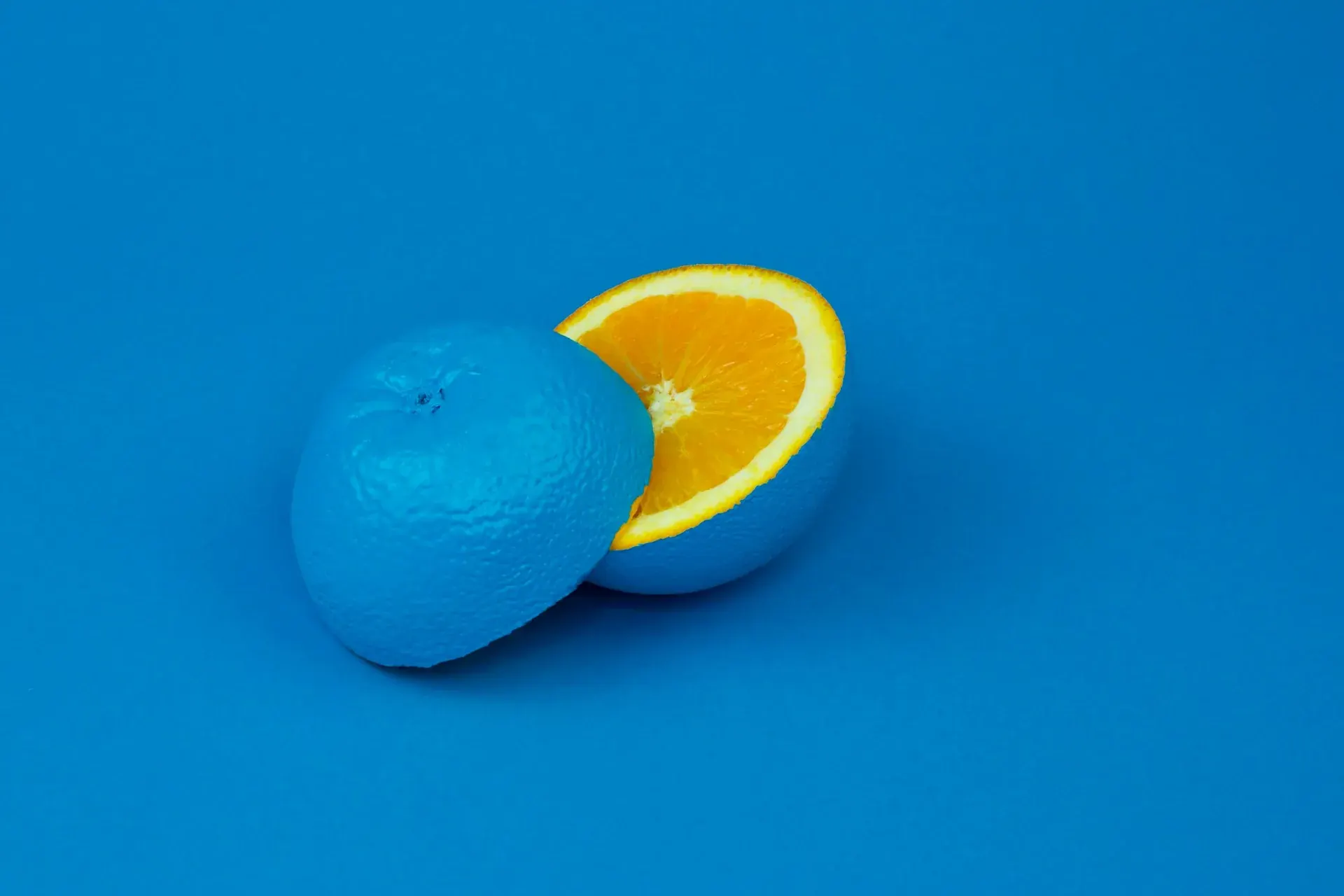 An orange cut in half, one half painted blue, on a blue background